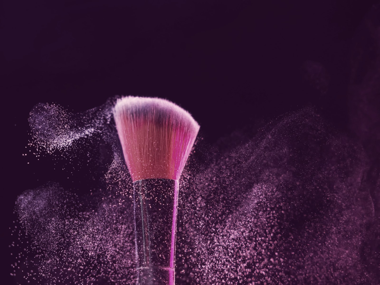 Makeup brush bursting with pigment powder against a dark background
