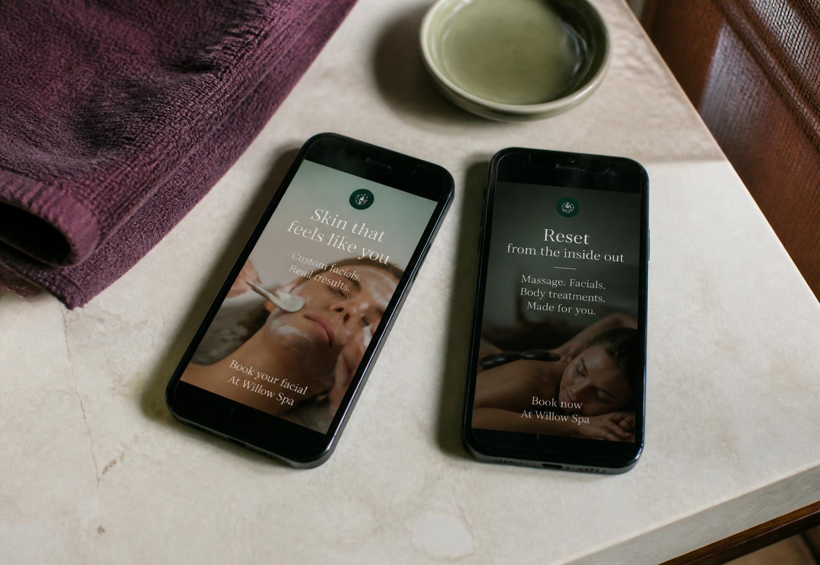 Two phones on a spa counter showing social ad creatives beside a plum towel and sage dish